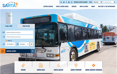 A SARTA public transit bus parked outdoors near another bus, with a digital trip planner and navigation menu visible on the website interface.