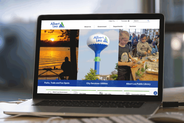 A laptop displays the Albert Lea city website, featuring sections for parks, utilities, and the public library, with related images and navigation menus.