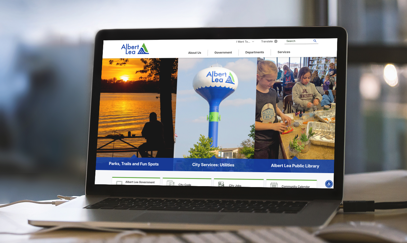 A laptop displays the Albert Lea city website, featuring sections for parks, utilities, and the public library, with related images and navigation menus.