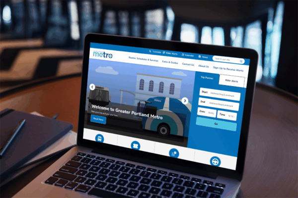 A laptop displays the Greater Portland Metro website with sleek website design, featuring route planning options and a homepage banner showing illustrated buses and buildings.