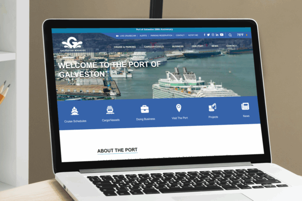 A laptop on a desk displays the Port of Galveston website, featuring a banner image of cruise ships docked at a port and navigation menus at the top.