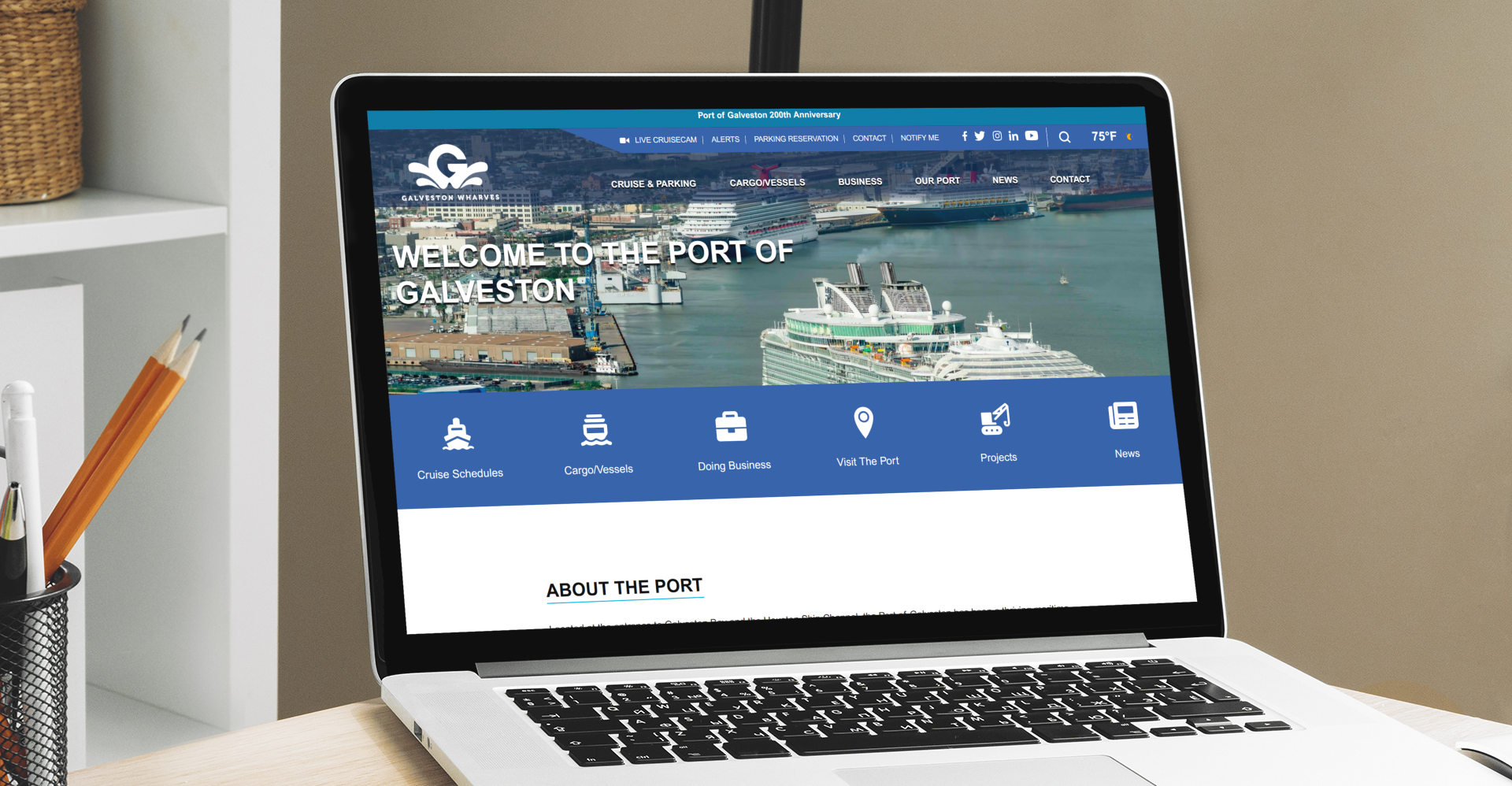 A laptop on a desk displays the Port of Galveston website, featuring a banner image of cruise ships docked at a port and navigation menus at the top.