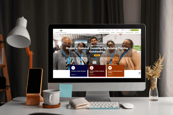 A desktop computer on a wooden desk displays a website featuring a group photo and text about building thriving communities. Office supplies, a lamp, and plants are also on the desk.