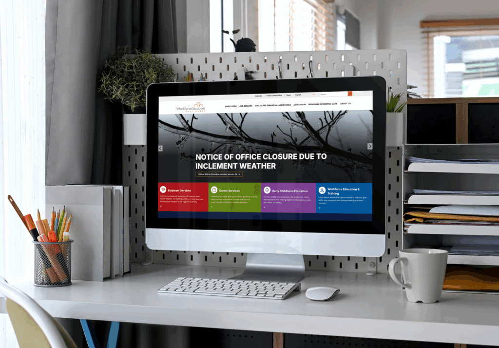 A computer on a desk displays a website with a notice that the office is closed due to inclement weather. Office supplies and a white mug are also on the desk.