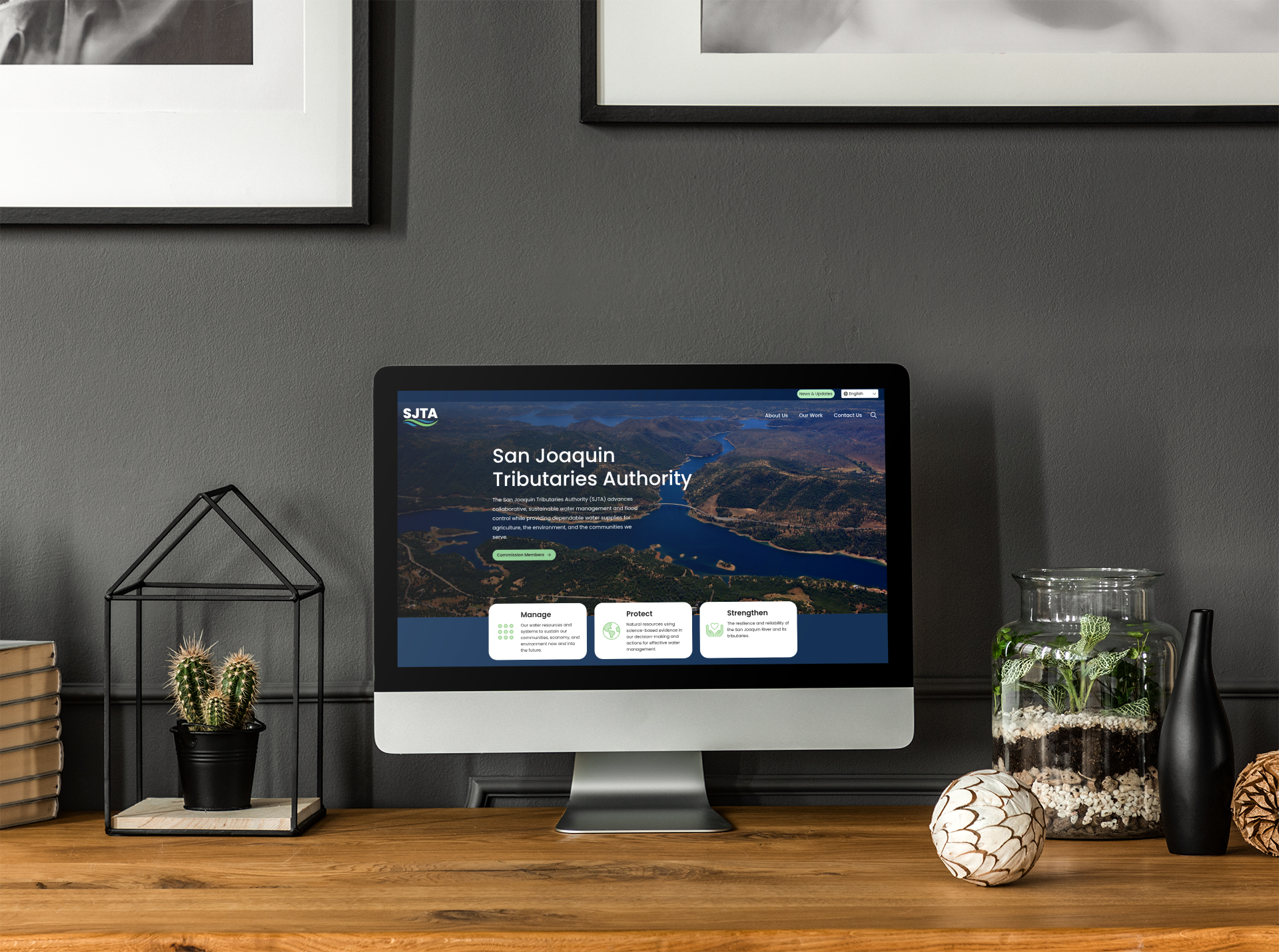 A desktop computer on a wooden desk displays the San Joaquin Tributaries Authority website; books, plants, and decorative items are also on the desk.