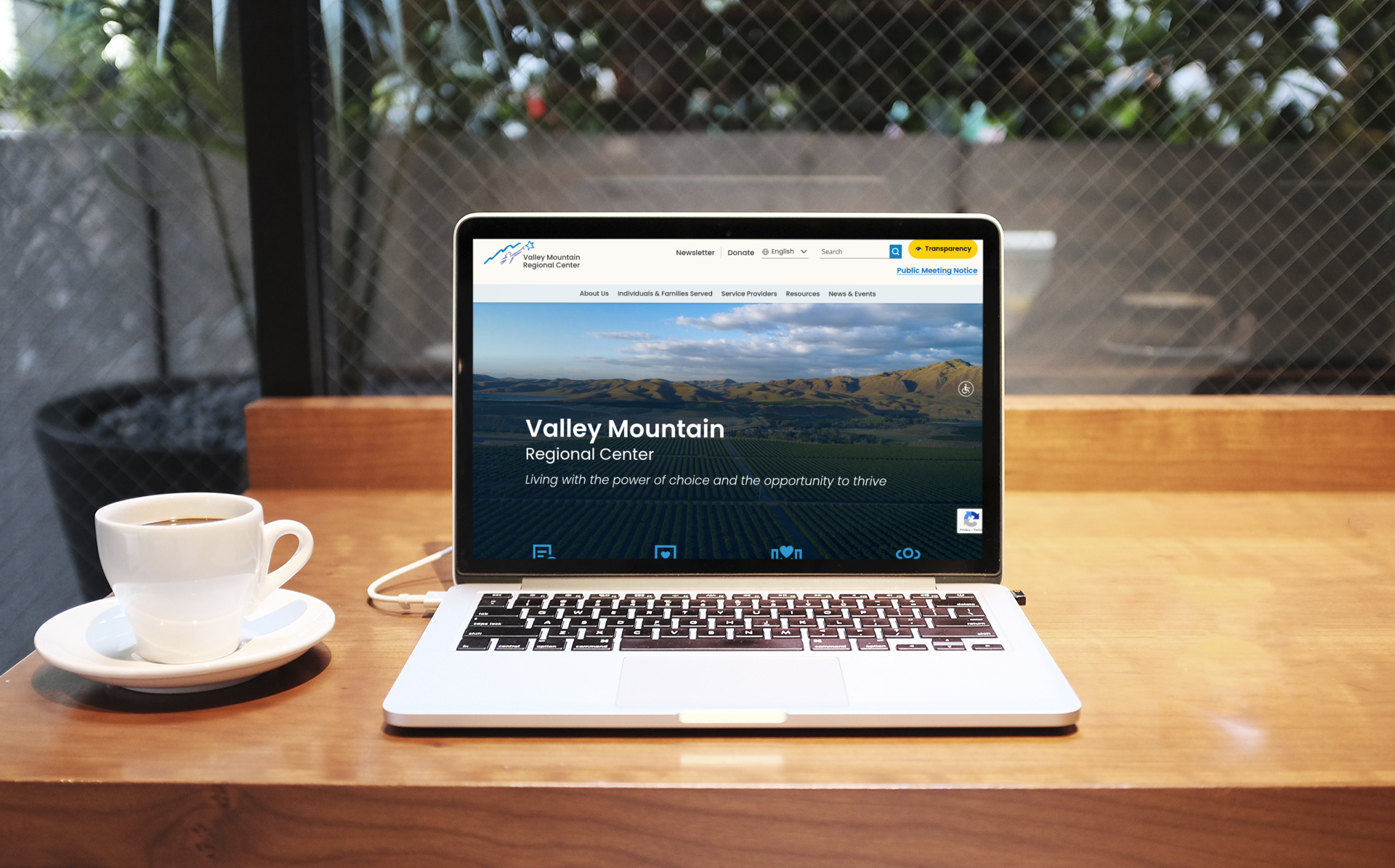 A laptop on a wooden table displays the Valley Mountain Regional Center website; a cup of coffee sits to the left.