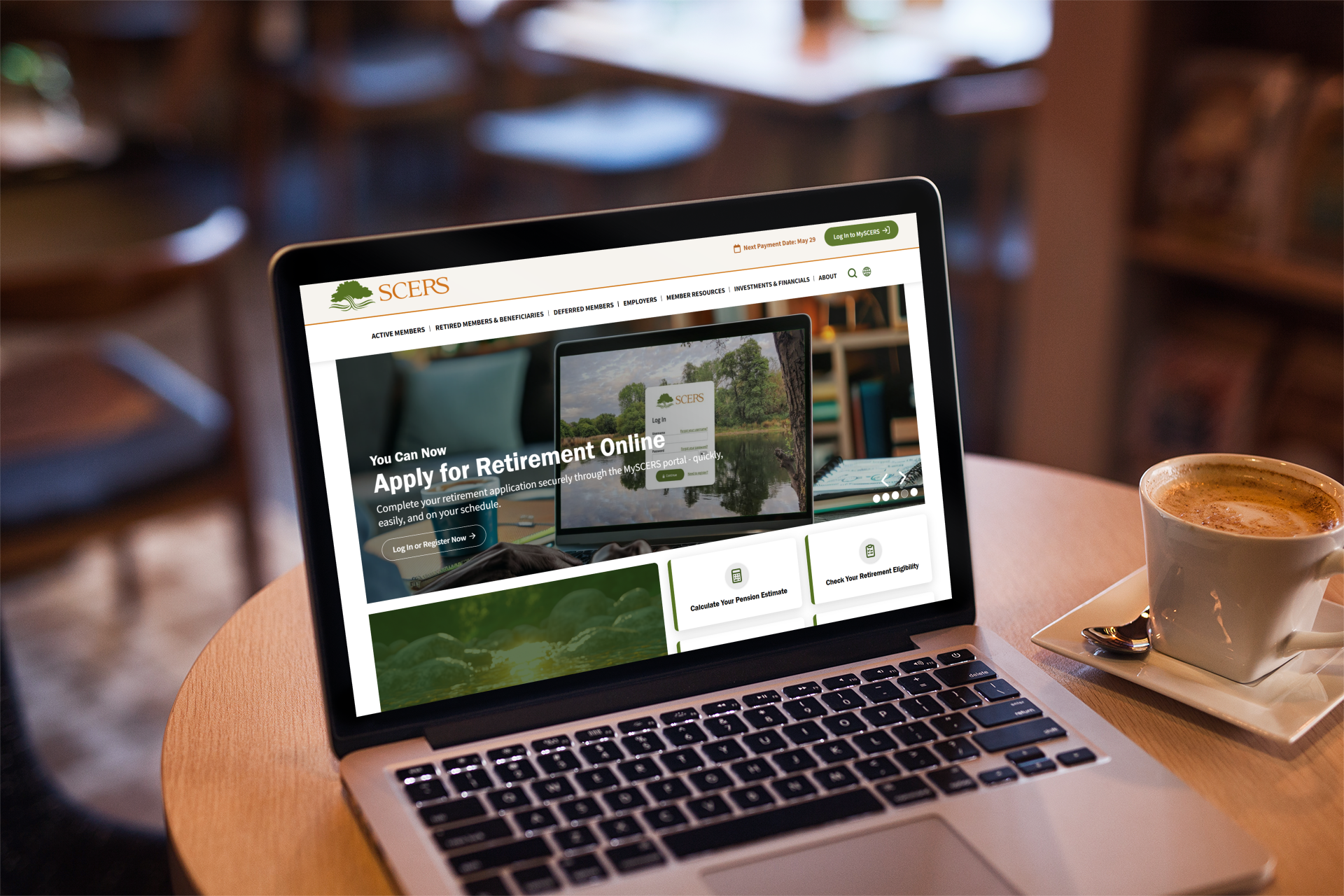 A laptop on a café table displays the SCERS website homepage, which features an option to apply for retirement online; a cup of coffee sits beside the laptop.