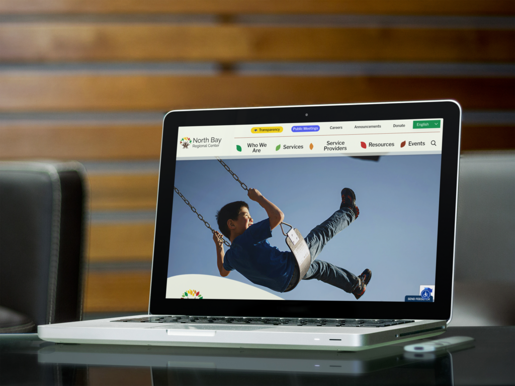 A laptop on a glass table displays a website homepage featuring a child swinging, with navigation links visible at the top of the screen.