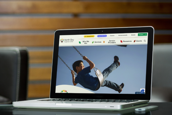 A laptop on a glass table displays a website homepage featuring a child swinging, with navigation links visible at the top of the screen.