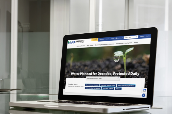 A laptop on a glass table displays a website about water resources, featuring a close-up photo of a plant with a water droplet and the headline 